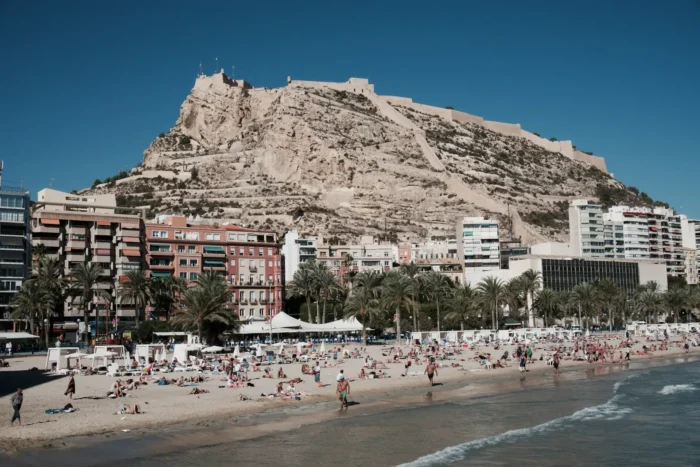 Vista panorámica de la Playa de San Juan en Alicante con palmeras, arena dorada y el mar Mediterráneo.